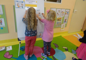 Dwie dziewczynki zawieszają na tablicy zasady z Kodeksu dobrych relacji.
